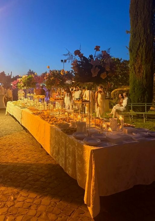 Tavolo imbandito per un matrimonio al tramonto, con ospiti in abito bianco, allestito da Delizie & Eventi